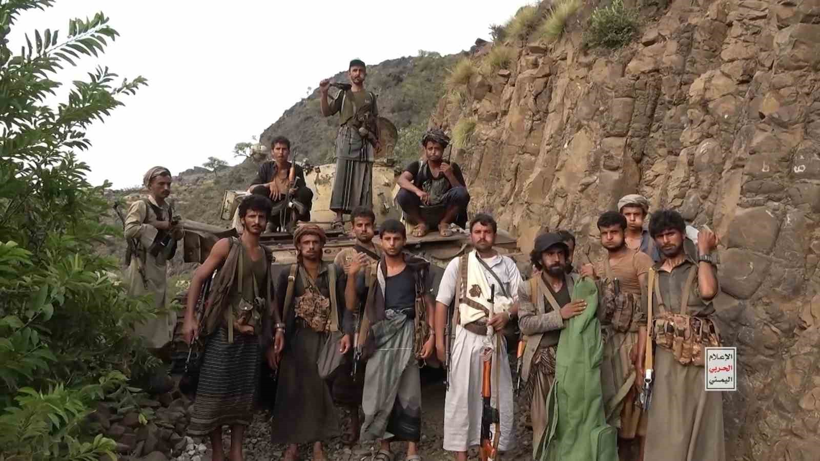 Dağlık bölgede silahlı kişilerin bir araç önünde toplu halde durduğu görüntü.