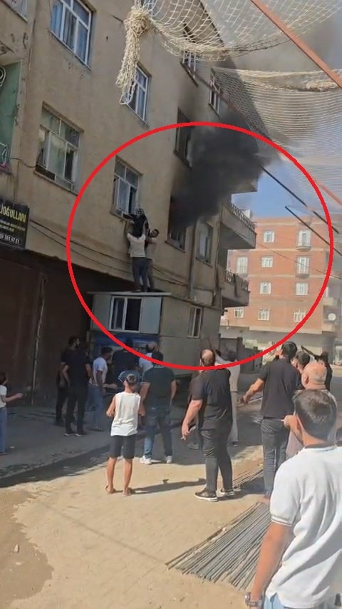 Bismil’de yangın çıkan binanın önünde toplanan vatandaşlar ve pencereden yükselen yoğun duman.