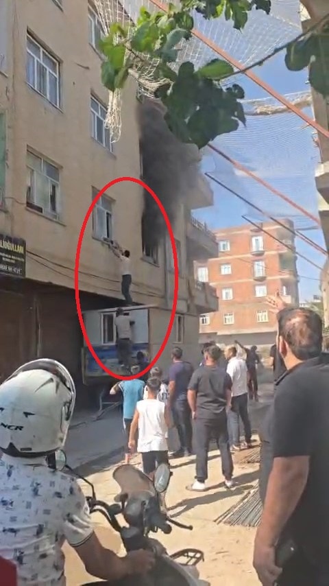 Binanın önünde toplanan kalabalık ve konteyner üzerinden pencereye ulaşmaya çalışan kişiler.