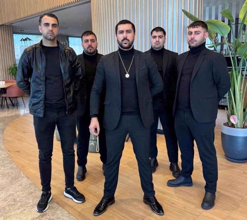 Siyah kıyafetli beş kişinin kapalı bir mekânda poz verdiği görüntü.