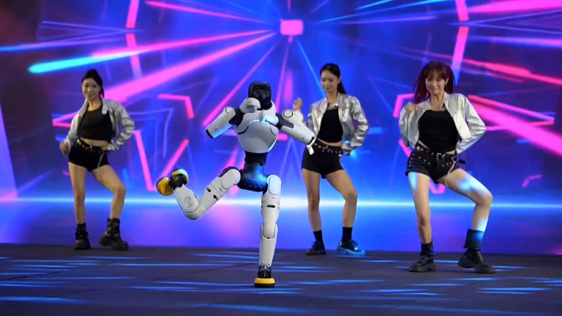 A humanoid robot dancing on stage with dancers in the background.
