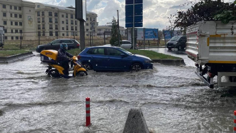 Vehicles and a motorcycle moving on a road with water accumulation after a downpour.