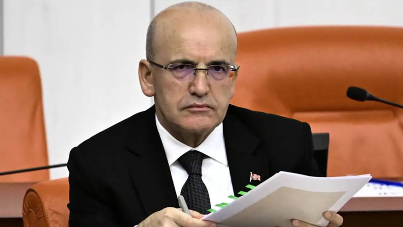 Mehmet Şimşek is seen in a meeting room with documents in his hand.