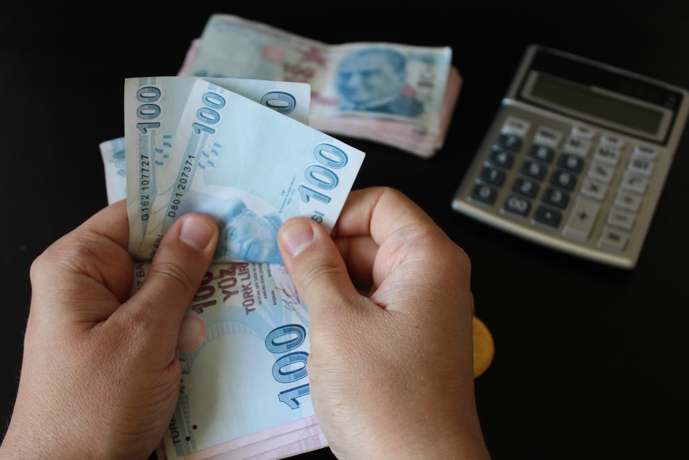 100 TL banknotes held in hand and a calculator in the background.
