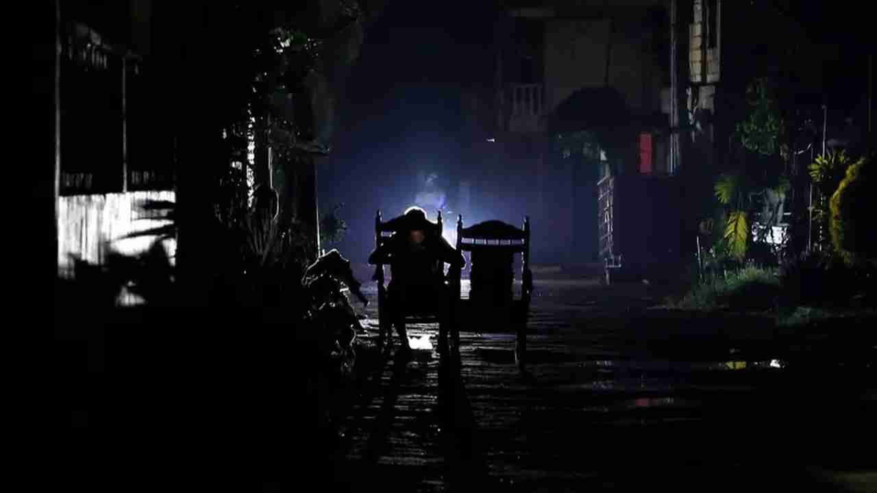 Chairs and building silhouettes visible under limited light on a dark street.
