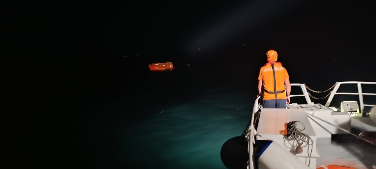 Gece karanlığında bir arama kurtarma teknesinden denizi tarayan görevli ve su üstünde görülen can kurtarma aracı.