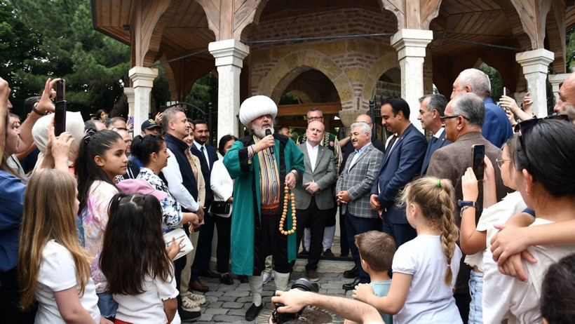 Müfit Can Saçıntı, Nasreddin Hoca kıyafetiyle kalabalık önünde mikrofonla konuşuyor.