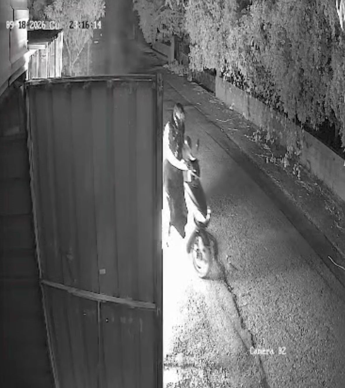 Night-vision camera footage shows a person on a motorcycle covered with a black bag next to the garage door.