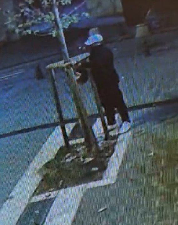 Security camera footage of a person standing next to a tree on the sidewalk during the night.