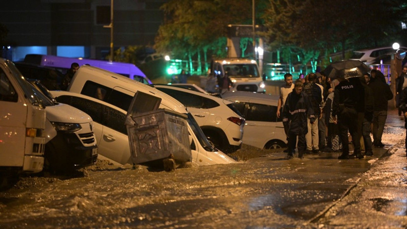 Sel sularının etkili olduğu sokakta araçlar ve olay yerindeki görevliler görülüyor.