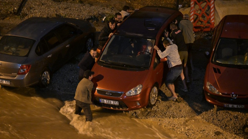Bir grup kişinin çamurlu zemindeki kırmızı aracı itmeye çalıştığı görülüyor.