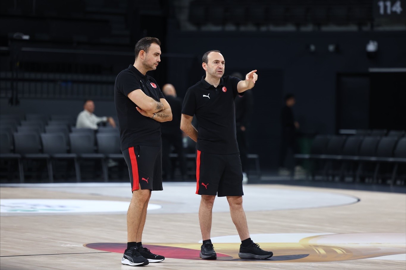 Ender Arslan ve bir teknik ekip üyesinin basketbol sahasında antrenman sırasında konuştuğu görüntü.