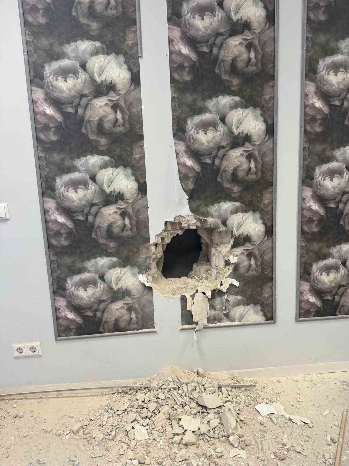 Çiçek desenli duvar kaplamasının üzerinde açılmış büyük bir delik ve yerde moloz yığını.