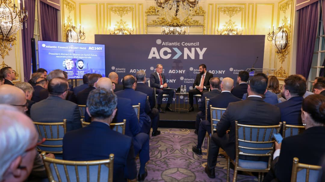 Speakers are seated on stage in a large hall at the Atlantic Council event.