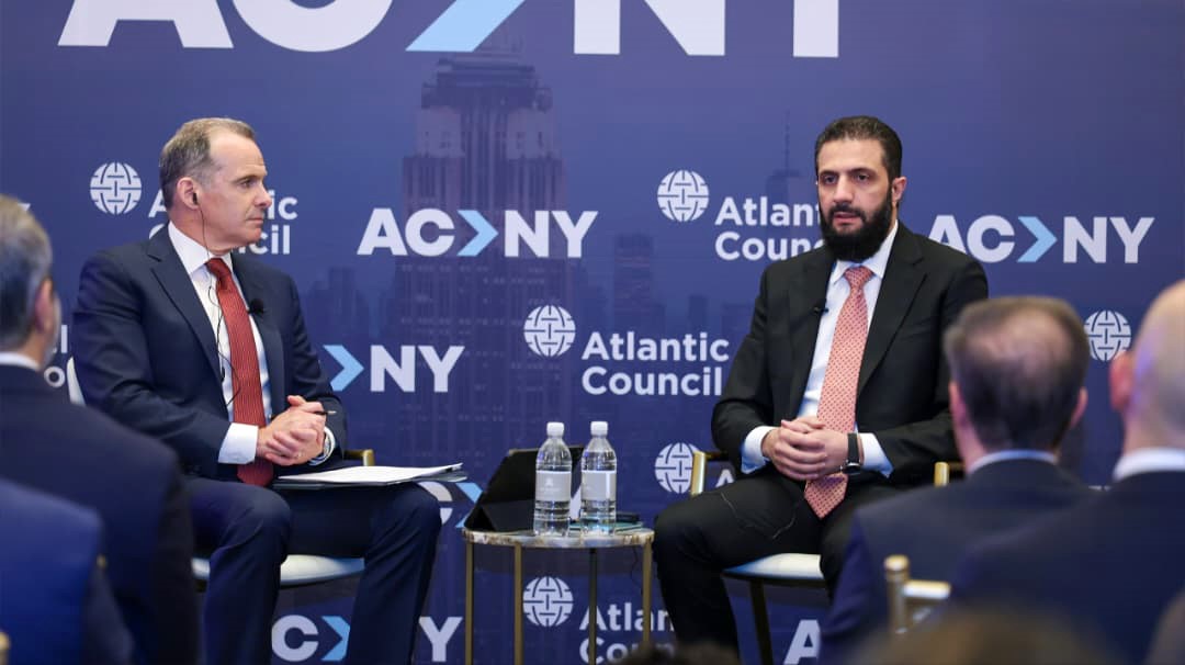 Ahmed al-Sharaa and the session moderator sit side-by-side on a stage featuring the Atlantic Council logo.