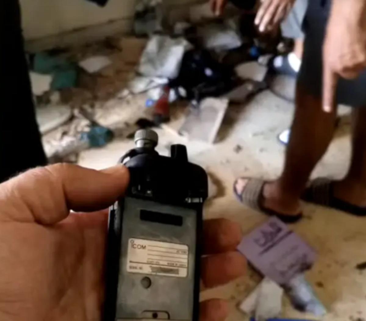 A walkie-talkie held in a person's hand with a cluttered interior in the background.