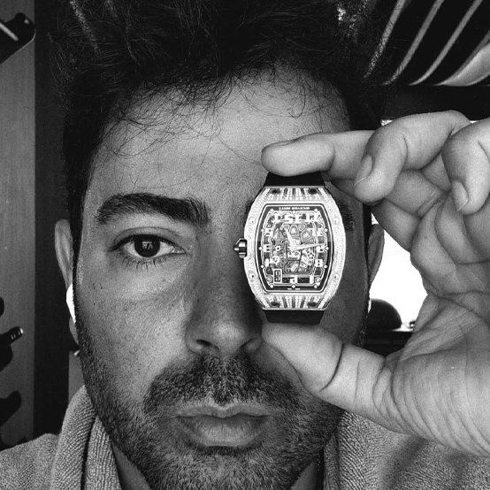 Ersan Gülmez’in elinde saat tuttuğu siyah beyaz yakın plan fotoğrafı.