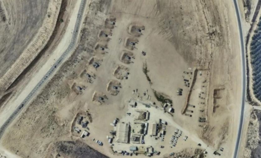 A large open area in the satellite image containing military vehicles, earthen barriers, and structures.