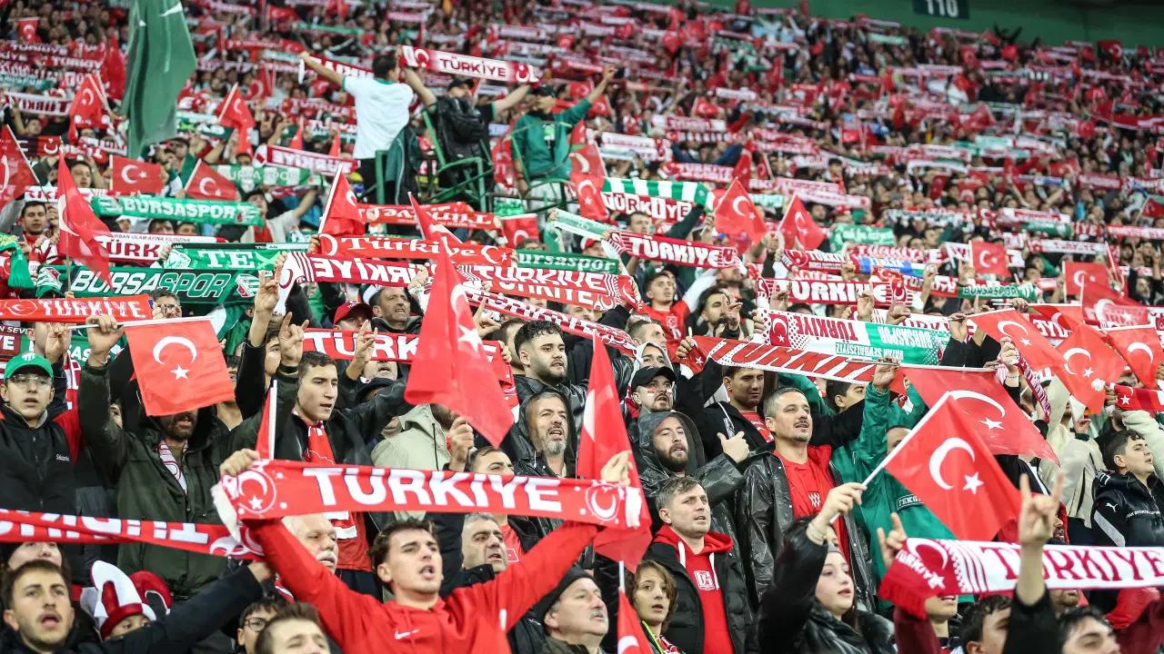 Türkiye bayrakları ve atkılarıyla dolu tribünlerde maçı izleyen taraftarlar.