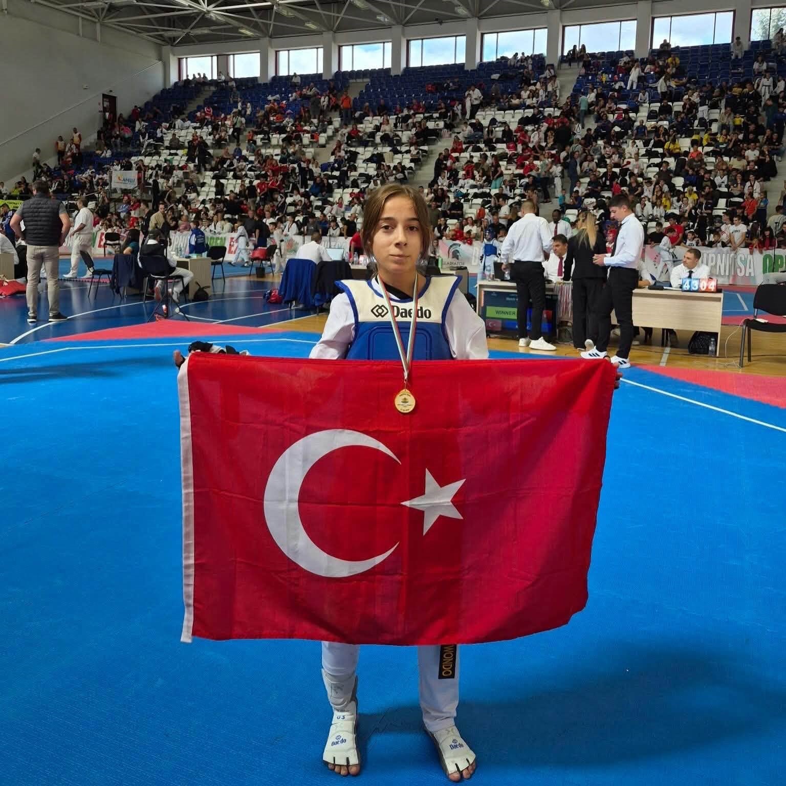 Taekwondo athlete Zeynep Acar from Bilecik holds the Turkish flag with her gold medal in the sports hall.