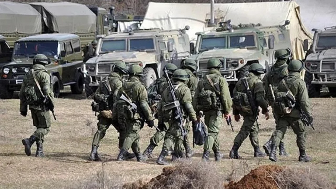 Soldados armados avanzando frente a vehículos militares.