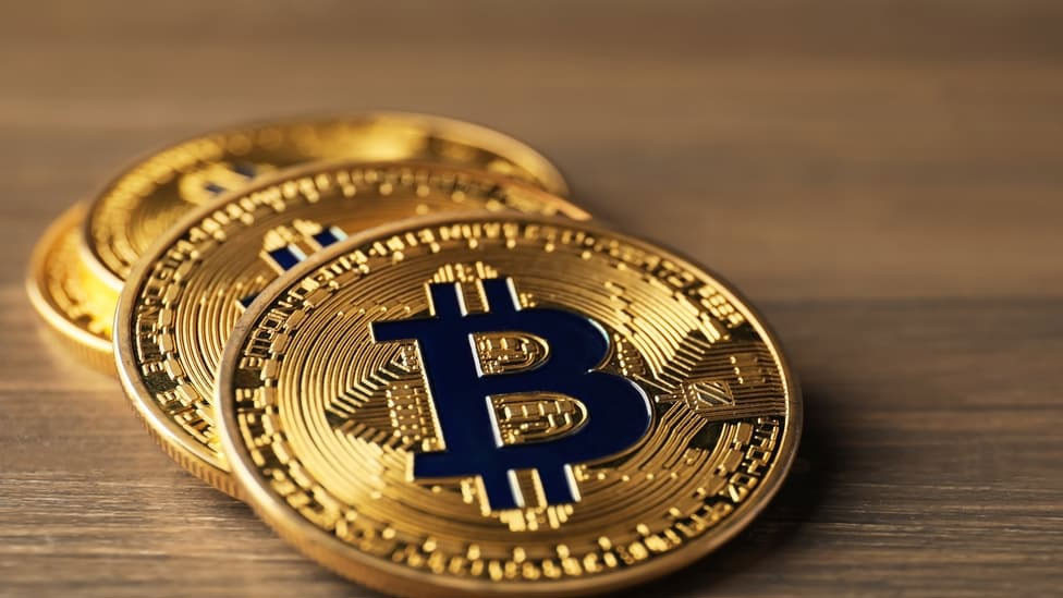 Ahşap zemin üzerinde birkaç Bitcoin temsili madeni para görseli.