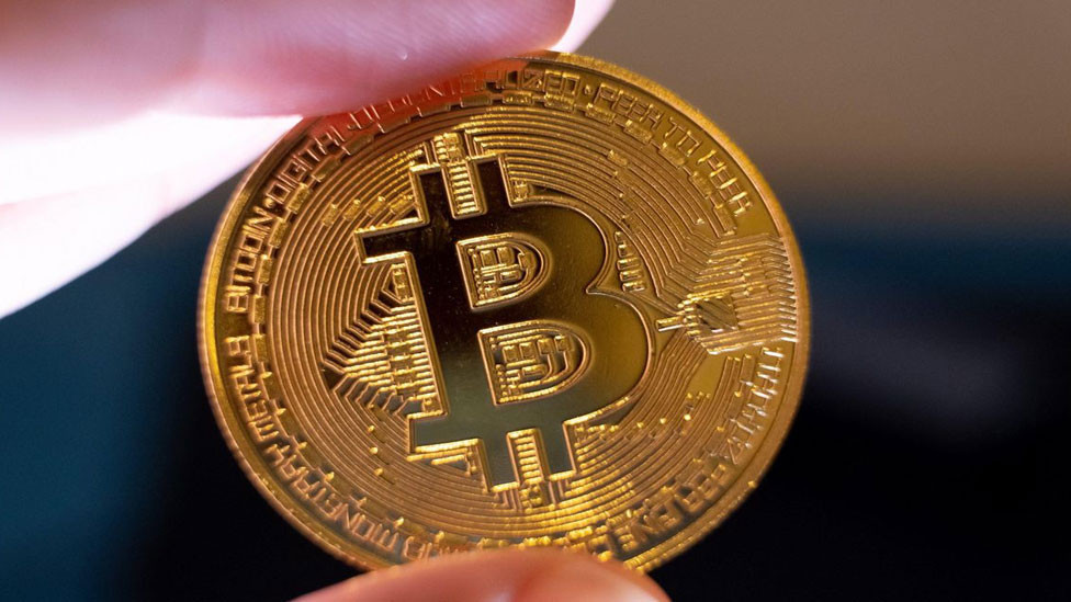 Parmaklar arasında tutulan Bitcoin temsili madeni para görseli.