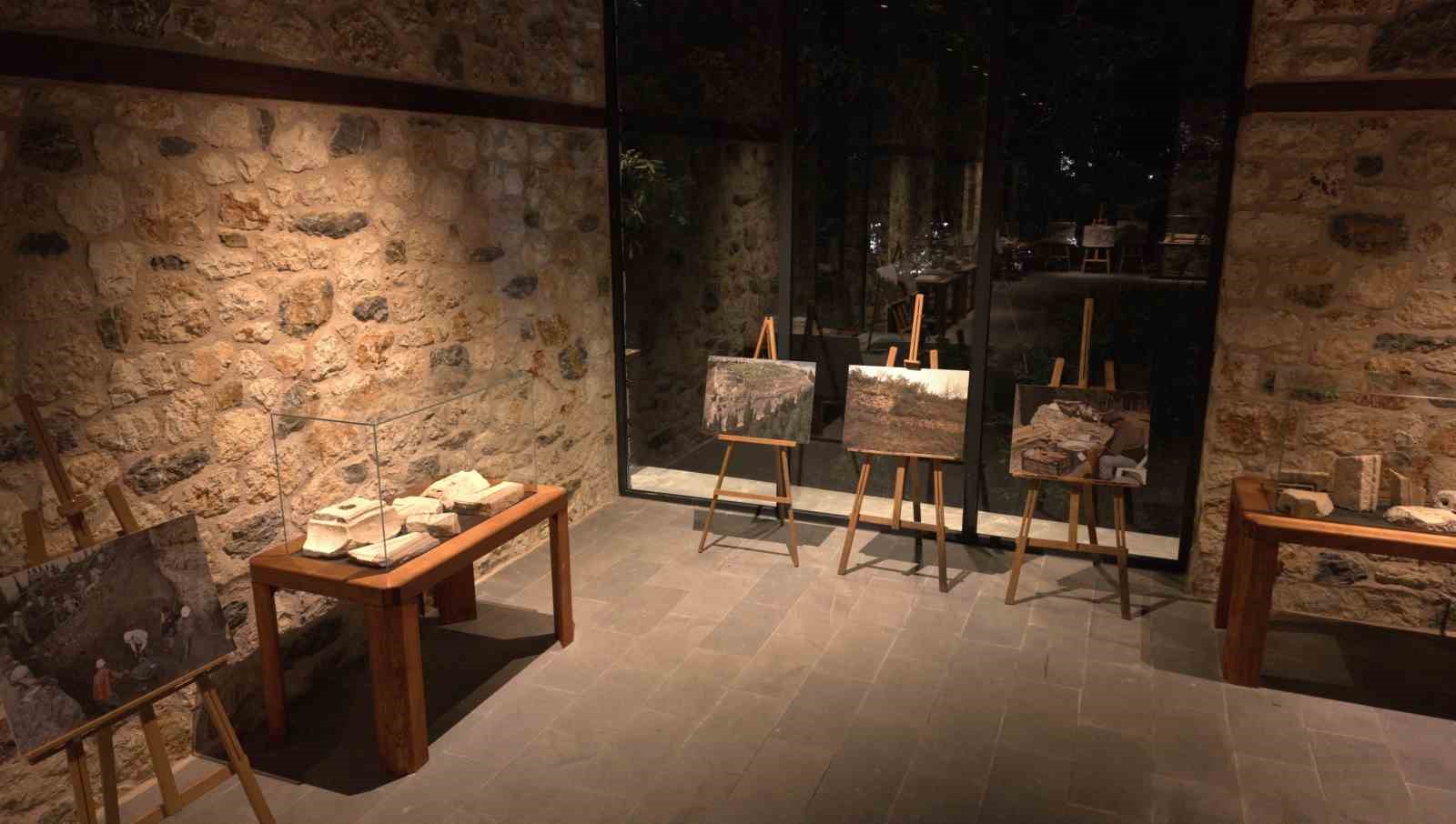 Aydos Müzesi içindeki sergi alanında vitrinler, taş eserler ve restorasyon sürecine ait fotoğraflar görülüyor.