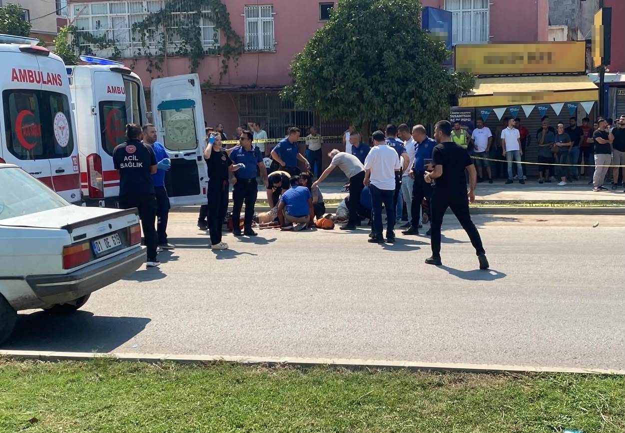 An ambulance, police, and people gathered around are seen at the scene following the armed attack in Adana.